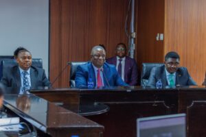 Sports Cabinet Secretary Salim Mvurya and Sports Principal Secretary Elijah Mwangi standing together at a parliamentary committee briefing, dressed in formal business suits while presenting the AFCON 2027 infrastructure budget proposal.