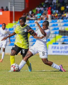 Two female youth football players from Kenya and Uganda fiercely contesting possession of the ball on the pitch during an international match.