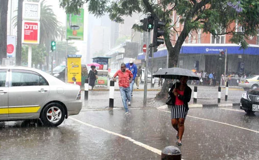 edestrians holding umbrellas walking along a busy Nairobi street during heavy rain with flooded pavements and vehicle traffic in the background.
